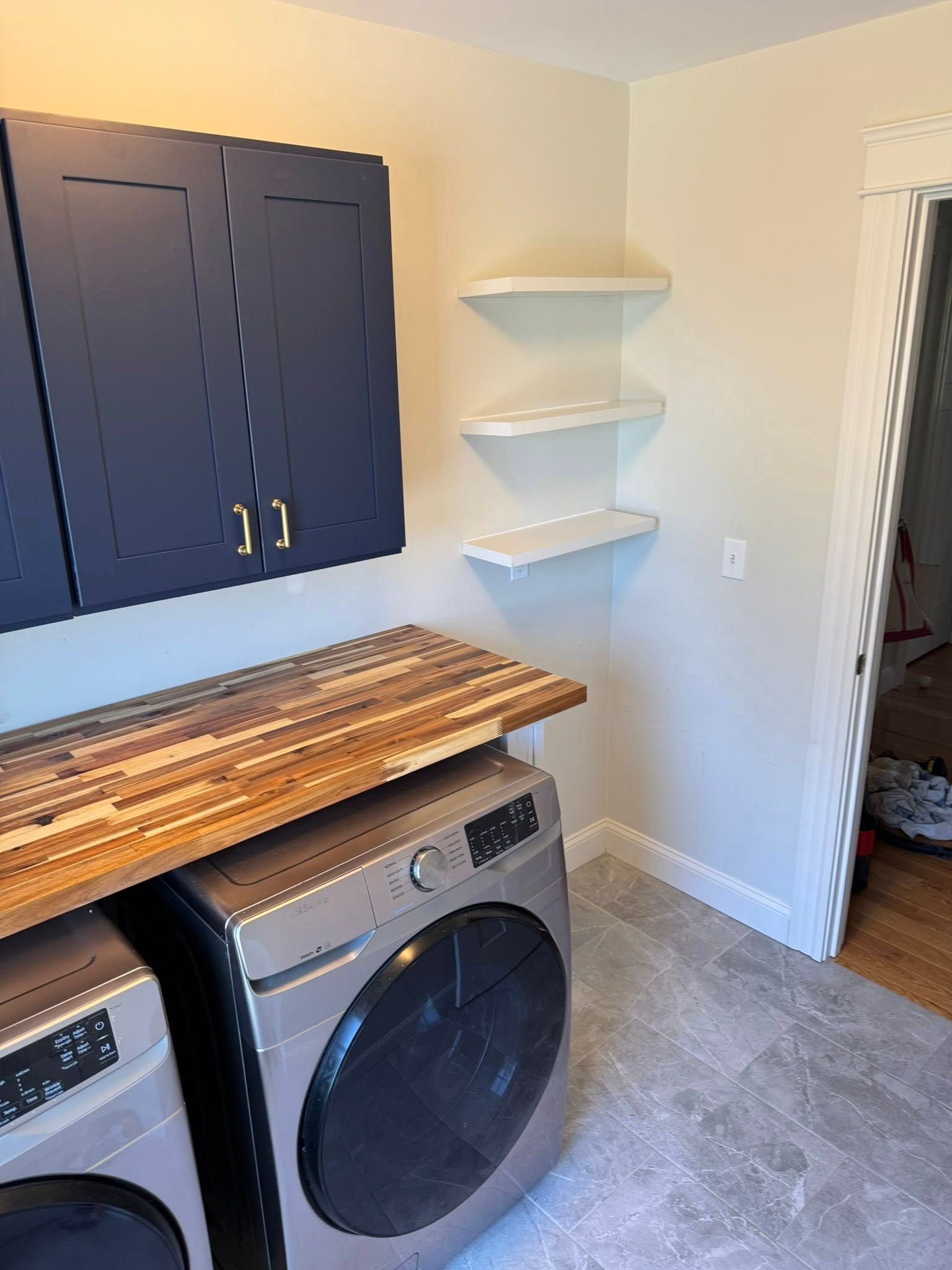 Laundry room with blue cabinets, washing machine, wooden countertop, and corner shelves.