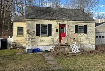 Dilapidated yellow house with peeling paint, black shutters, red door, and overgrown yard.