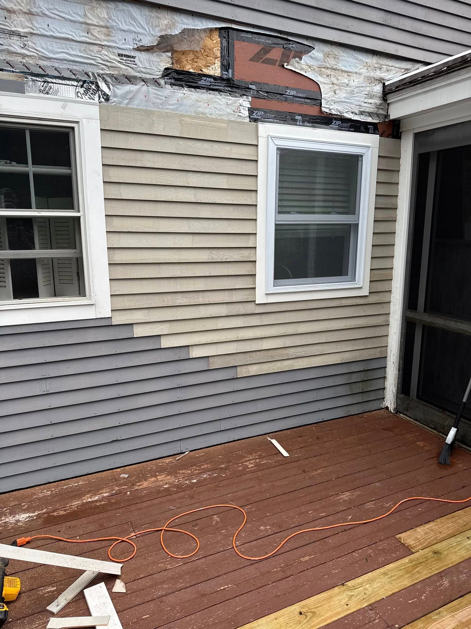 Exterior of a house with damaged siding above a wooden deck. Exposed wood and insulation visible.