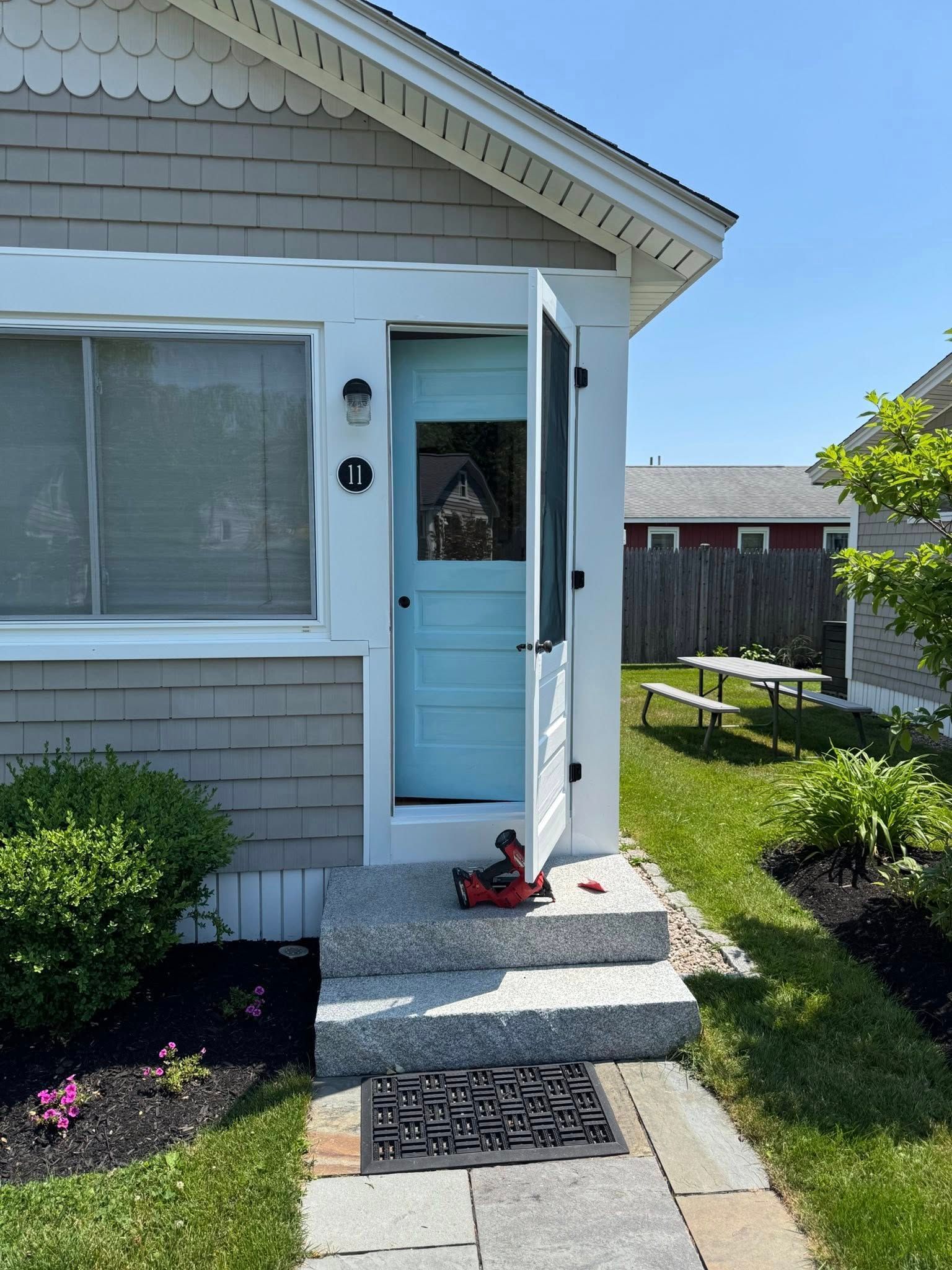 Light blue door and screen door open at a small home with grey siding, on steps with granite and a doormat.
