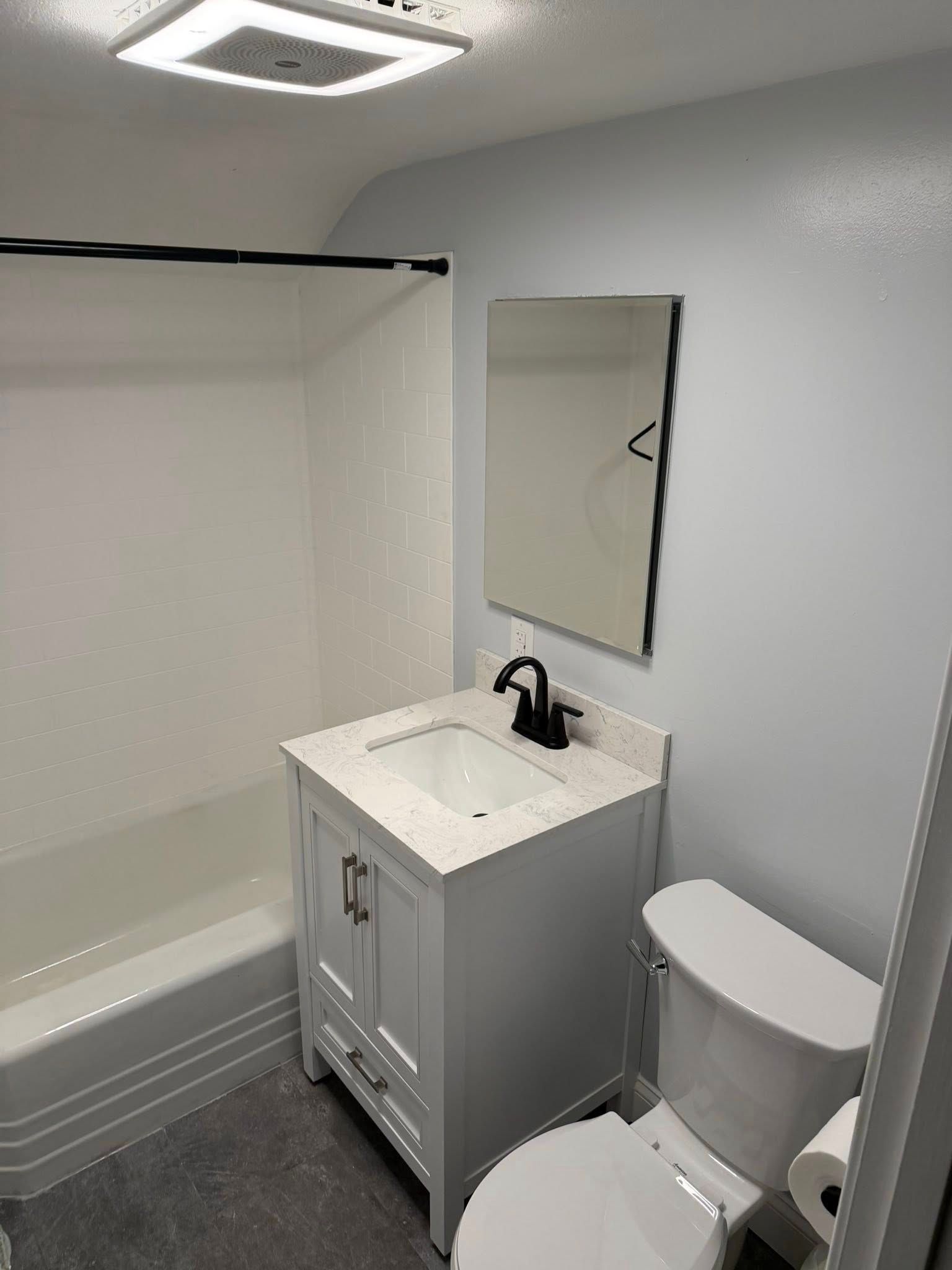 Bathroom with white vanity, toilet, and bathtub; gray floor and light blue walls.