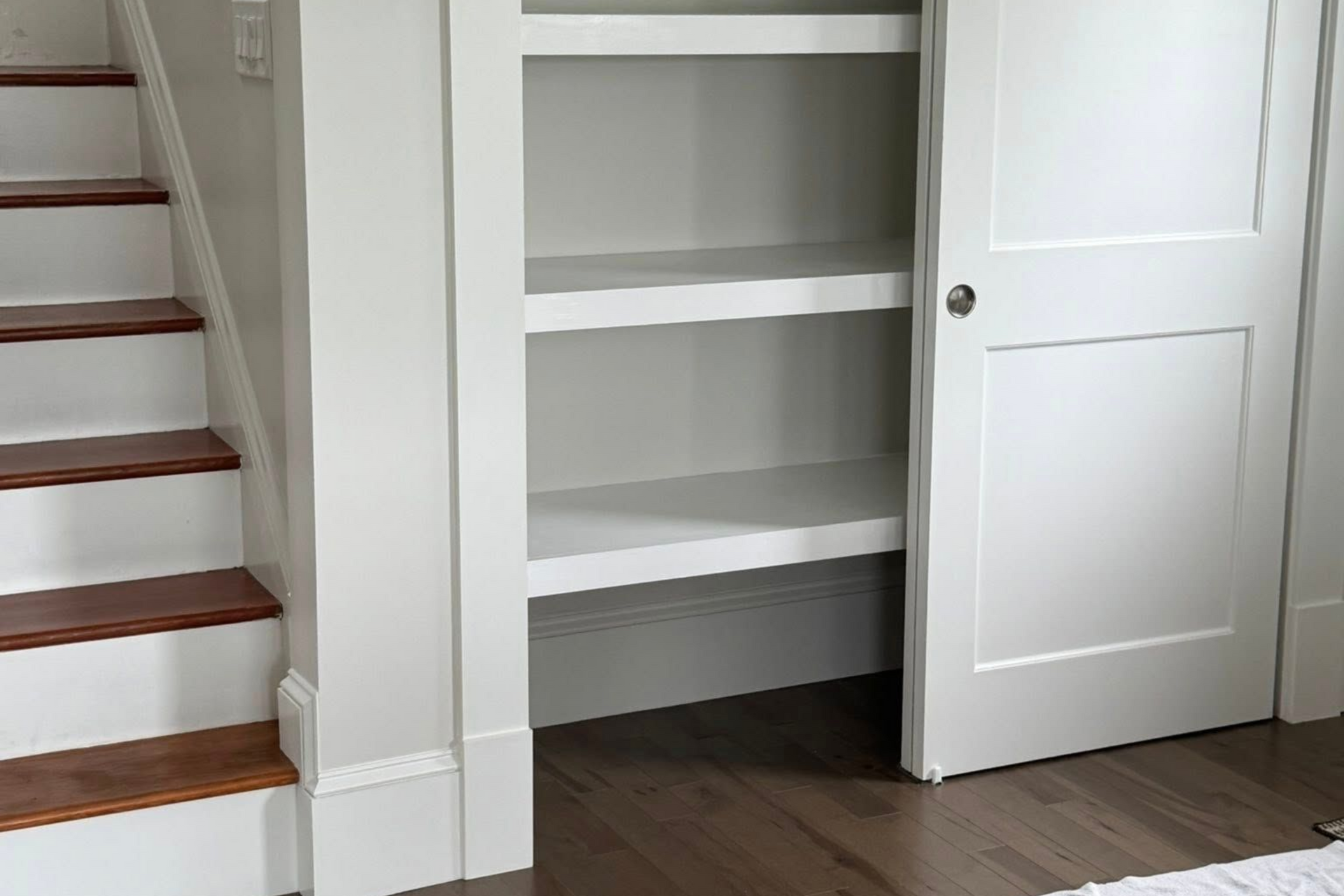 Staircase and white built-in shelving inside a closet. Door to the right is partially open.