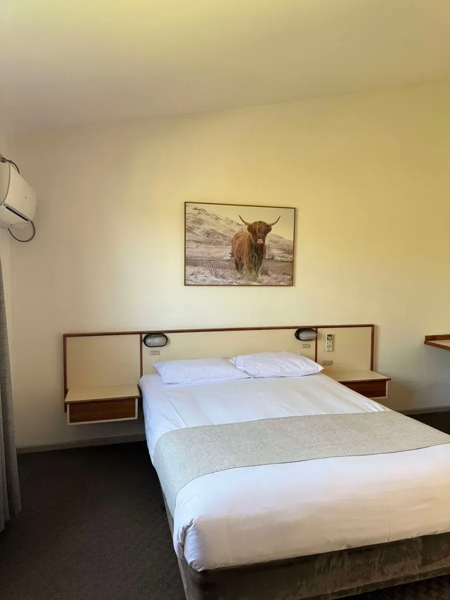 A Hotel Room With a Neatly Made Bed and a Painting Hanging on the Wall — Country Comfort Gin Gin Wild Scotsman Motor Inn in Gin Gin, QLD