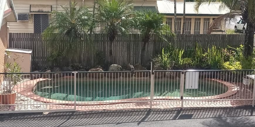 A Swimming Pool Surrounded by a Fence and Trees in Front of a House — Country Comfort Gin Gin Wild Scotsman Motor Inn in Gin Gin, QLD