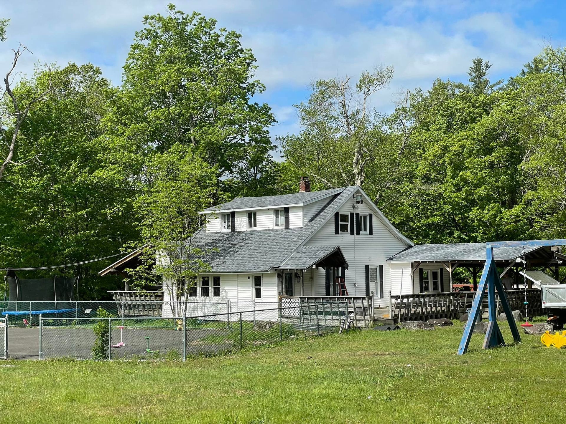 A white house with a gray roof is surrounded by trees and a playground.