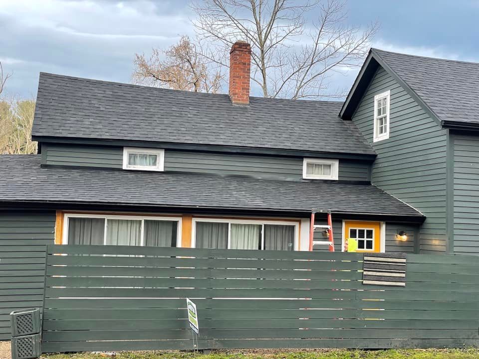 A green house with a black roof and a wooden fence in front of it.