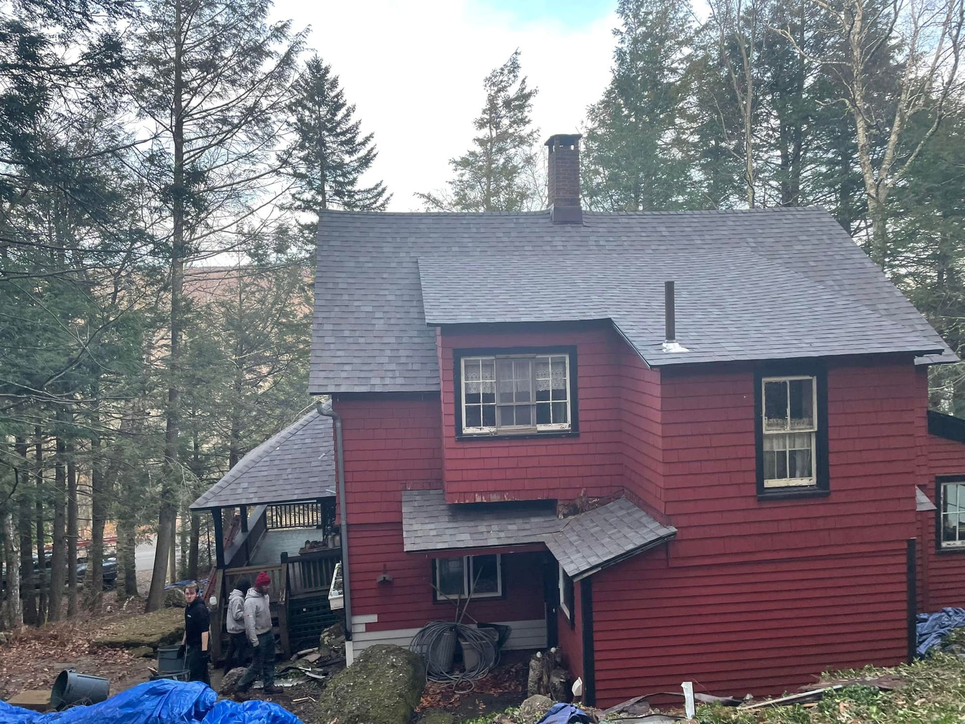 A red house with a black roof is surrounded by trees