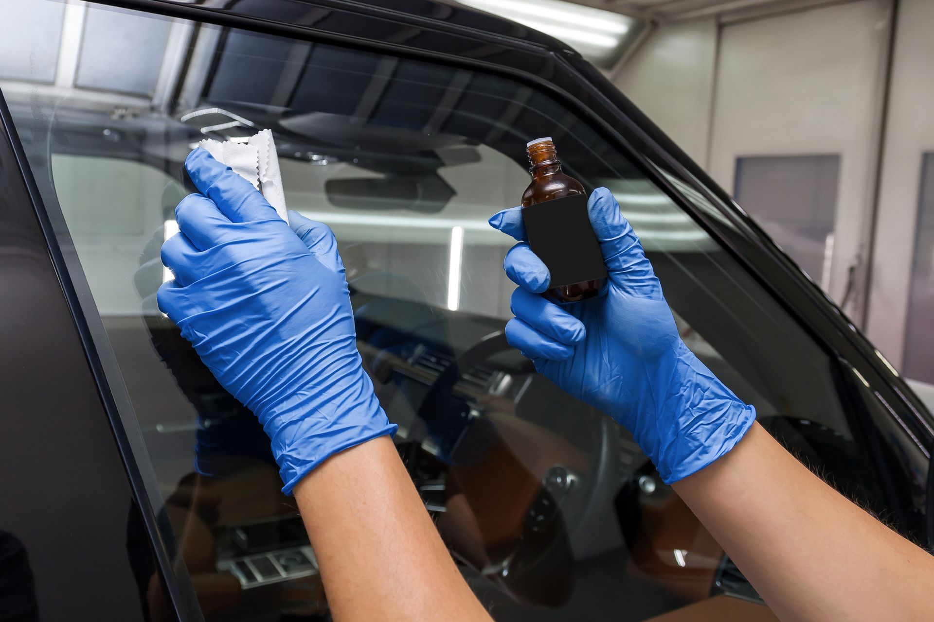 A person wearing blue gloves is cleaning the windshield of a car.