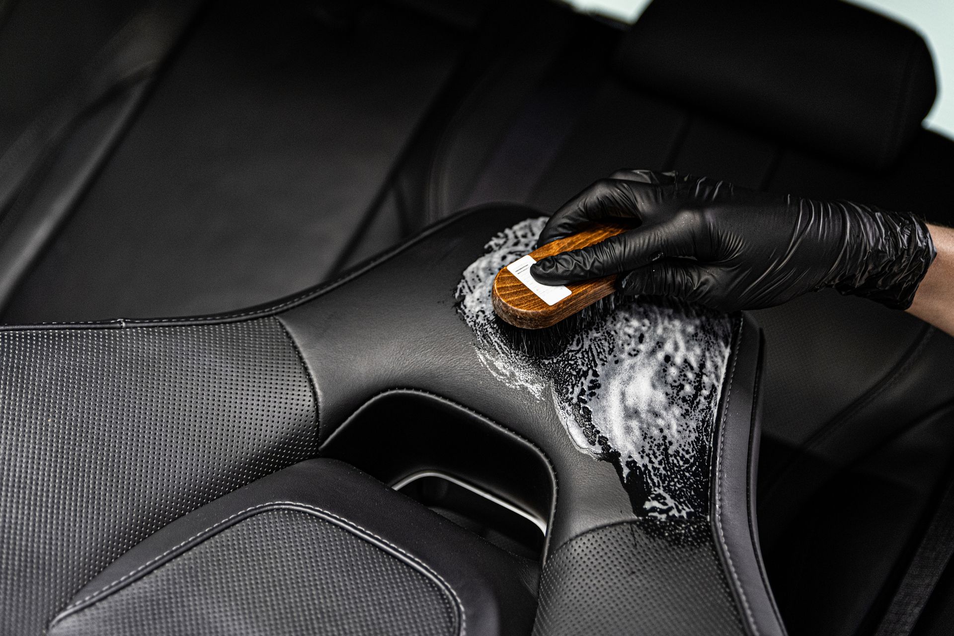 A person is cleaning a leather seat in a car with a sponge.