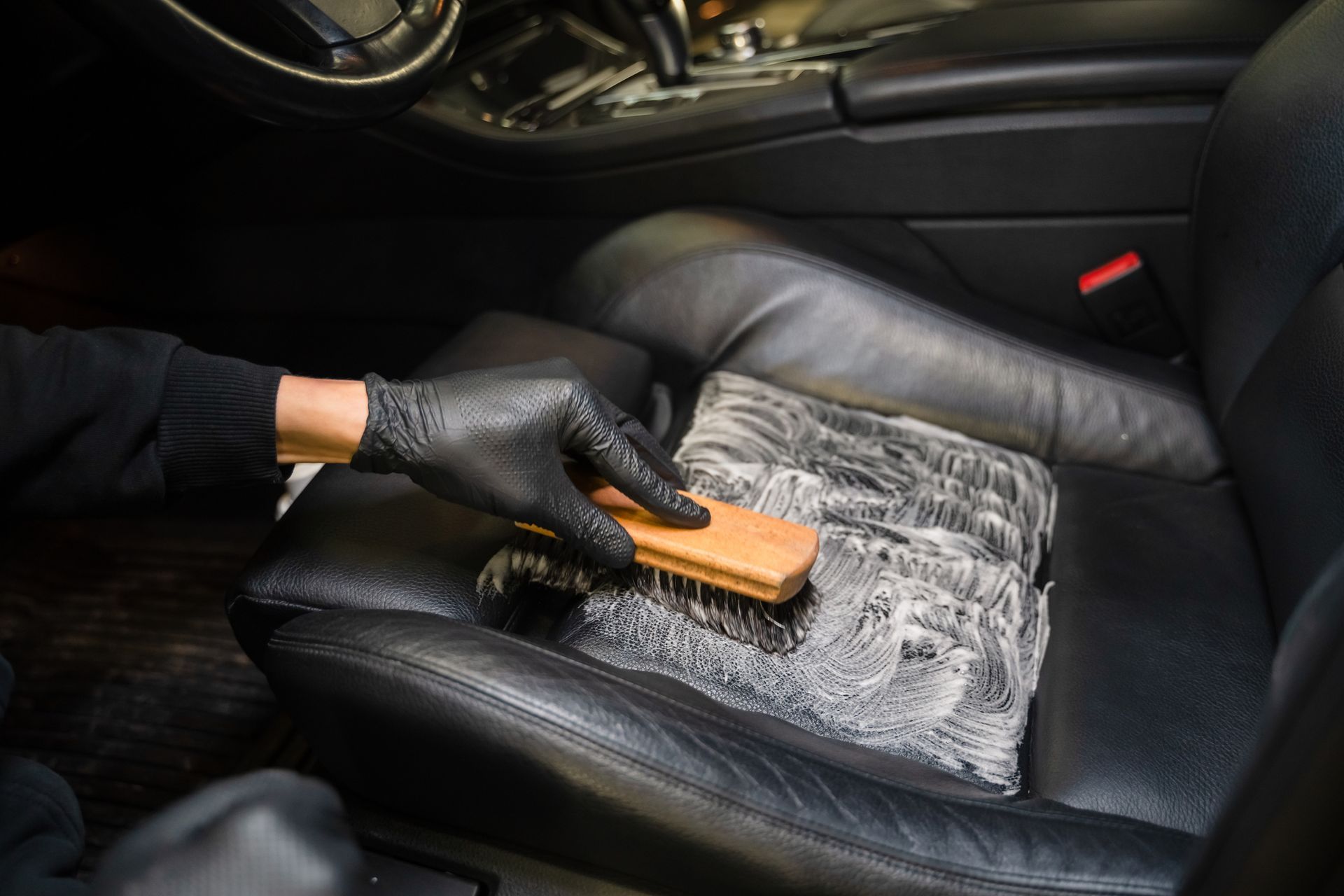 A person is cleaning a leather car seat with a brush.