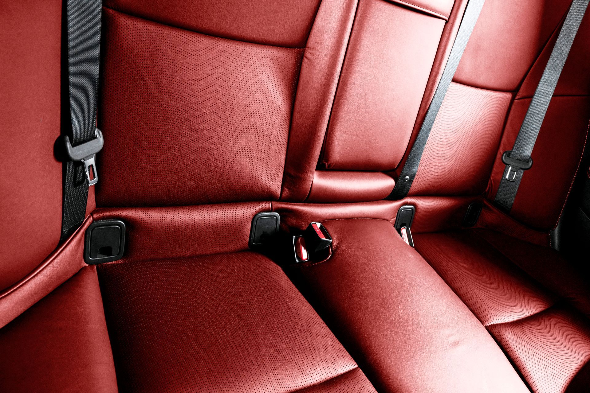 The back seat of a red car with black seat belts