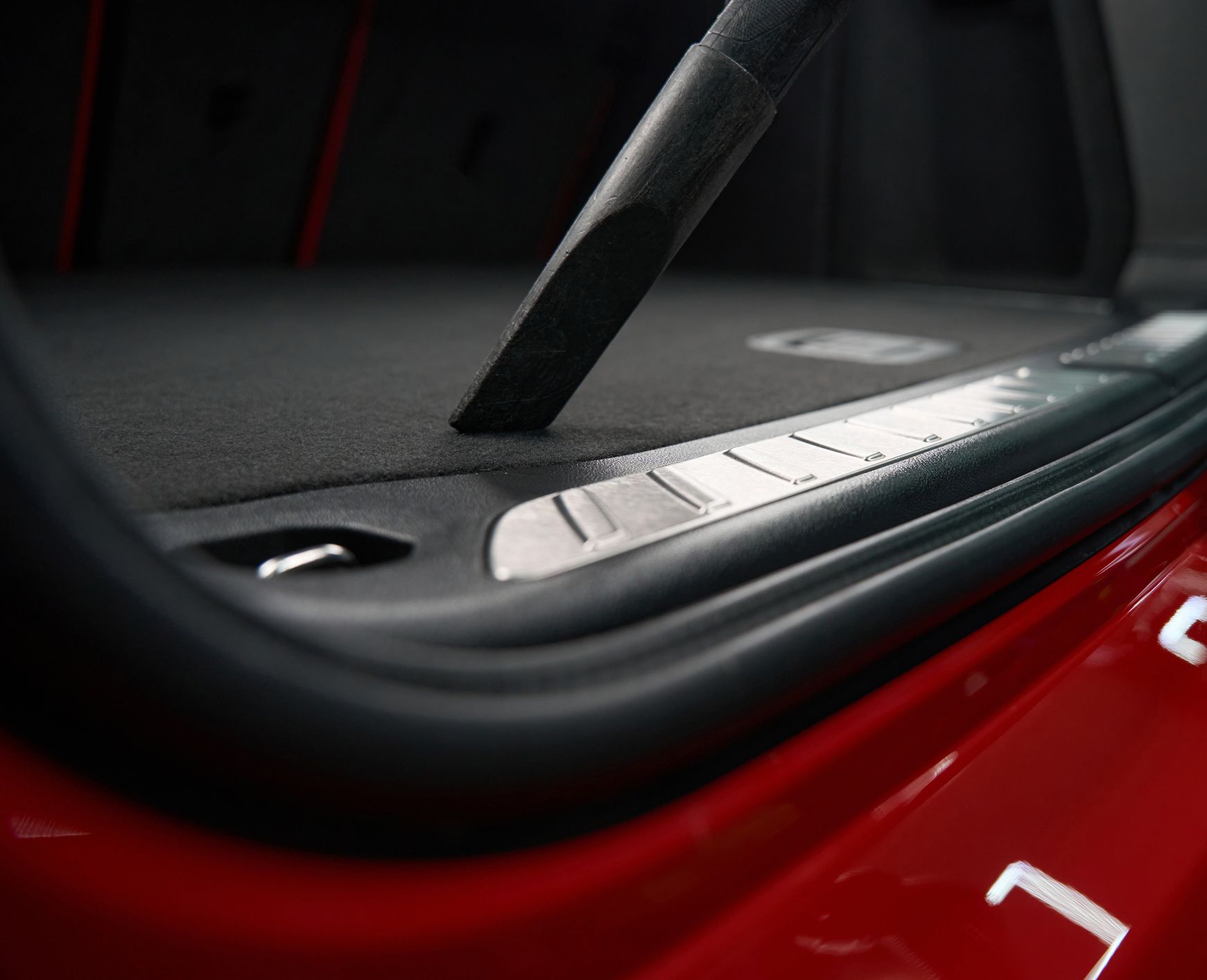 A vacuum cleaner is cleaning the trunk of a red car