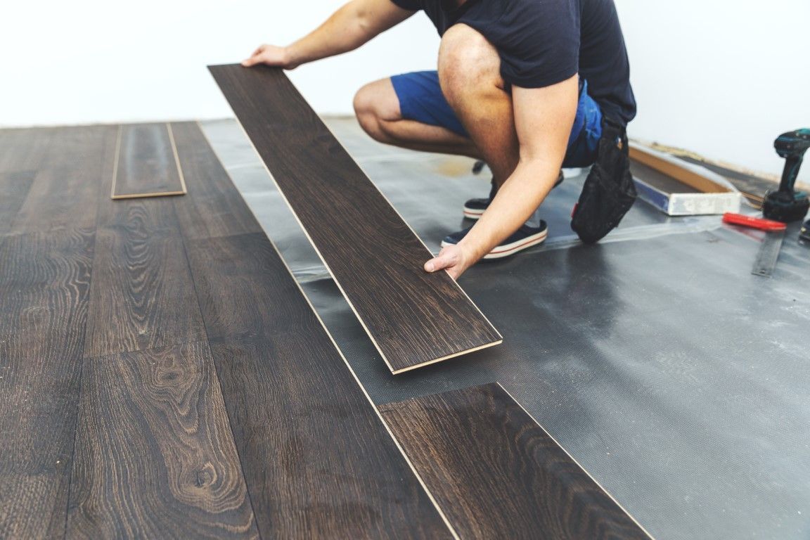 Person installing dark wood flooring, kneeling on a gray subfloor.