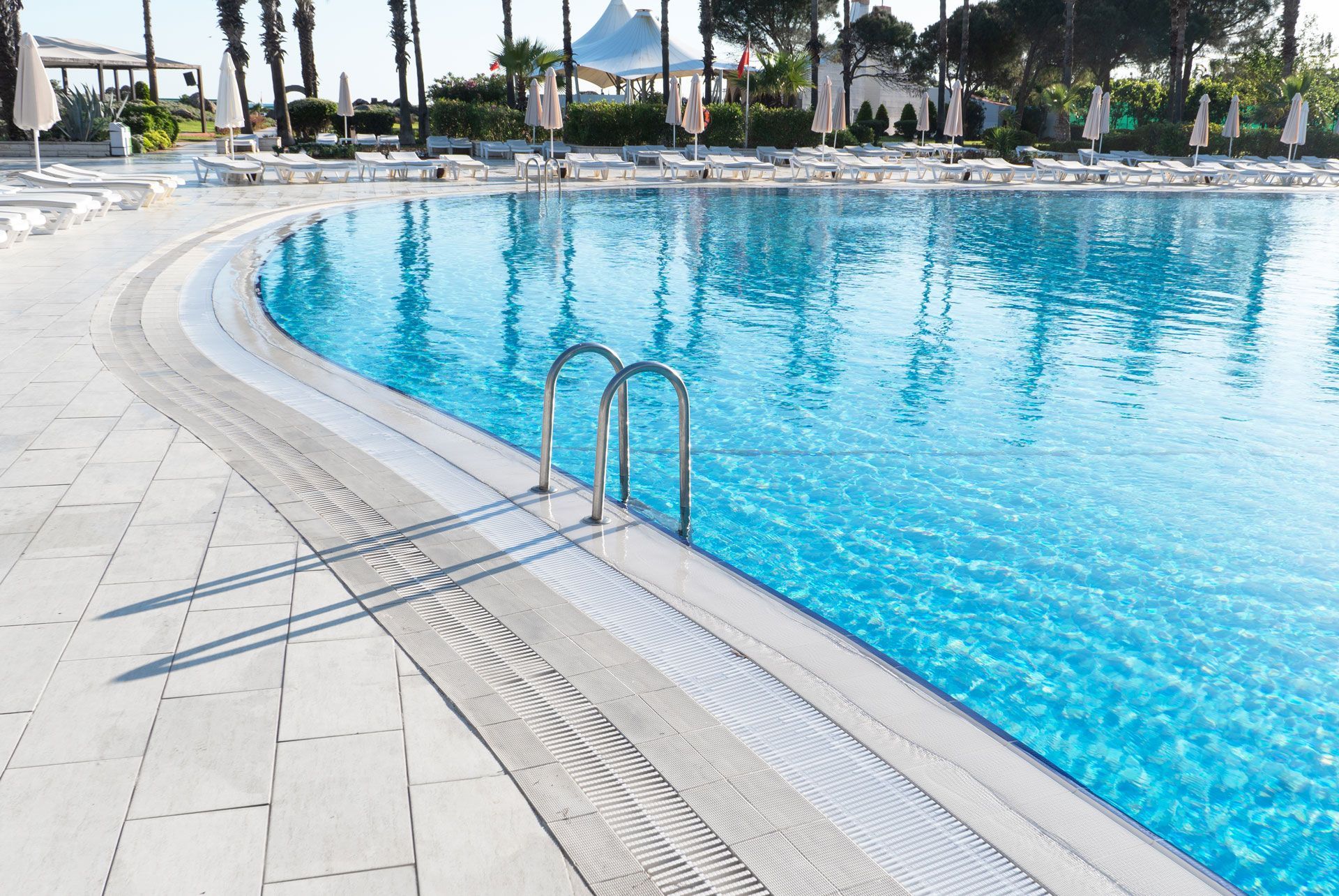 Swimming pool with clear blue water and curved edges, surrounded by white tiles and lounge chairs.