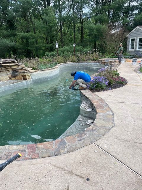 White patio with rectangular pool, small house and large house, blue water and sky.