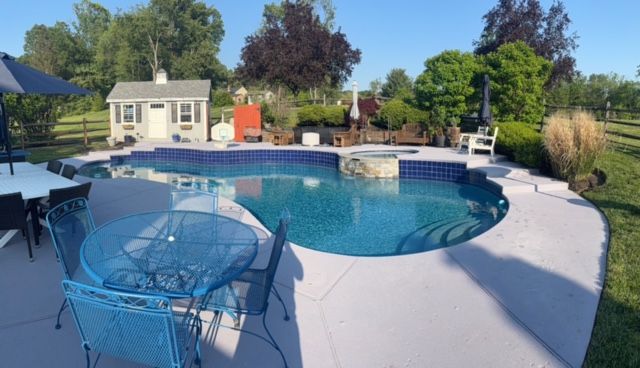 Pool with a dark blue interior, surrounded by light concrete patio.