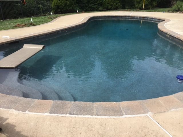 Blue swimming pool with attached hot tub, brick border, and scattered debris.