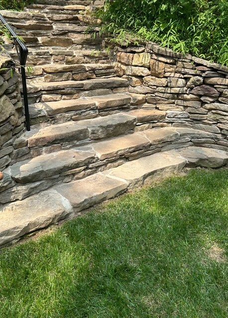 Person swimming in a small outdoor pool surrounded by stonework and wooden decking; trees in the background.