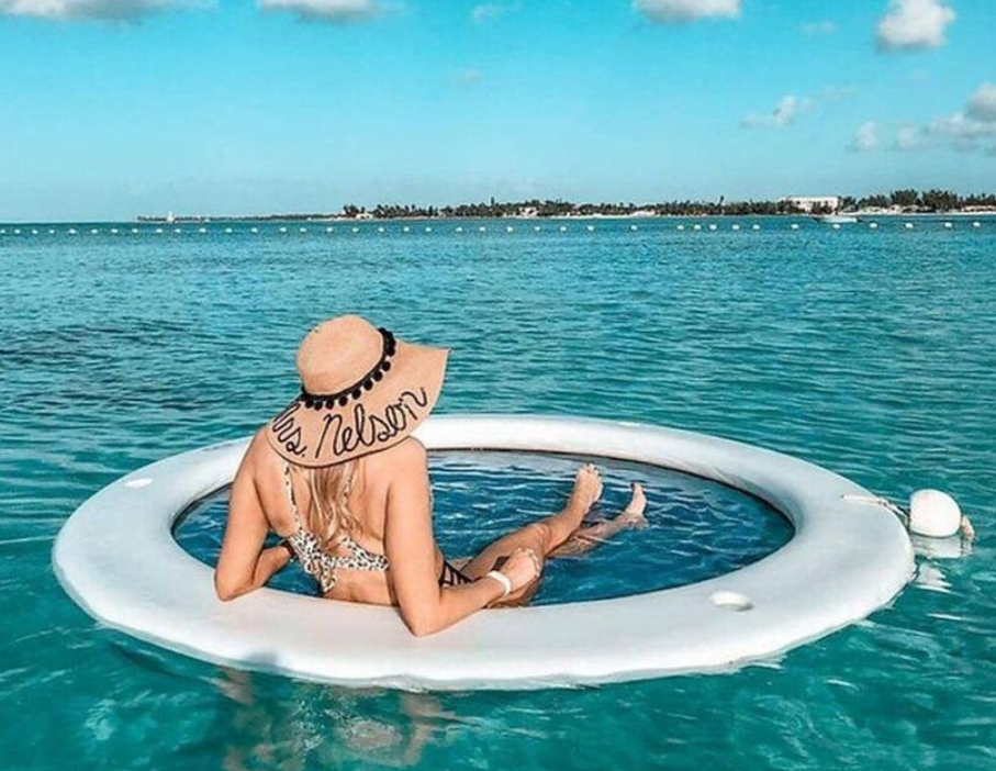 Woman in a hat sits in an inflatable pool in clear blue ocean water, enjoying the view.