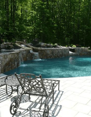 Swimming pool with stone waterfall and ornate metal chair on a patio.