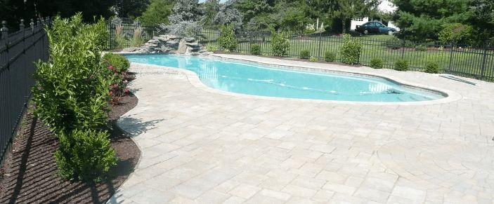 Swimming pool surrounded by stone patio and lush landscaping.