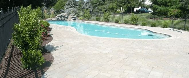 A long, winding swimming pool with light-colored stone pavers surrounding it.