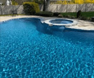 A blue swimming pool with an attached hot tub in a backyard setting, reflecting sunlight.