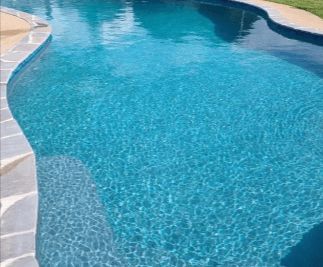 Blue swimming pool with stone edging, rippling water.