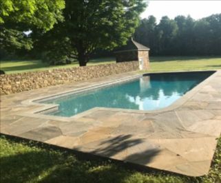 Swimming pool with stone patio, stone wall, and trees in a grassy area.