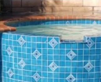 Blue tiled hot tub with decorative diamond tiles, brick surround, and water.