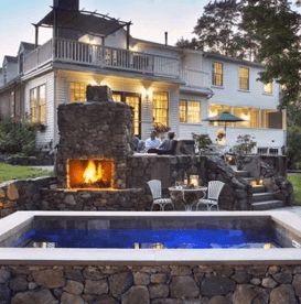 Stone fireplace and pool with a white house in the background; outdoor gathering.