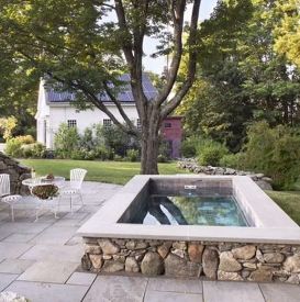 Backyard with stone-lined hot tub, patio, white furniture, green lawn, and a white house in the background.