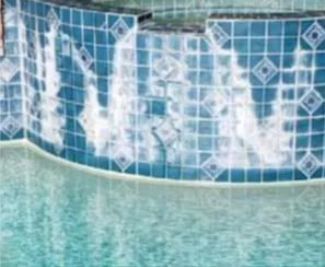 Pool tiles with water cascading over them. Blue and white tiles with diamond pattern at the top, light blue water.