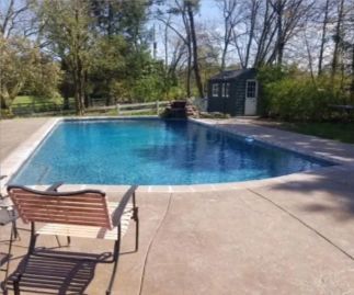 Swimming pool with bench, waterfall, and shed in a sunny backyard setting.