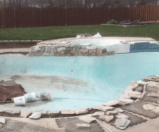 Empty swimming pool undergoing renovation, with rock features and debris visible.