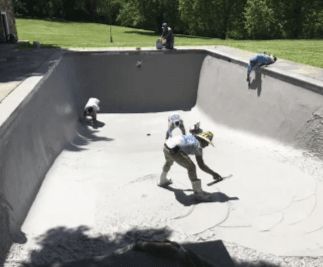 Workers applying a gray coating to the interior of a concrete swimming pool on a sunny day.