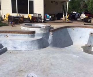 Empty swimming pool with a raised hot tub, backyard setting.