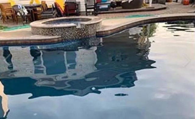 Swimming pool with adjacent hot tub; house reflected in water; outdoor setting.