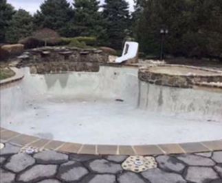 Empty outdoor pool with stone border and landscaping in the background.