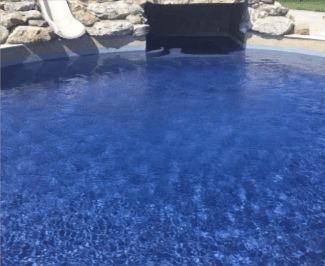 Blue tiled swimming pool with a water slide and rock feature.