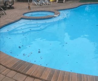 Blue swimming pool with attached hot tub, brick border, and scattered debris.