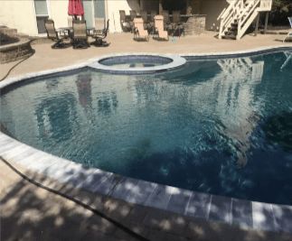 Swimming pool with jacuzzi, surrounded by patio furniture and stairs, outdoors.