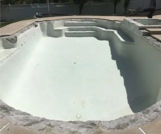 Empty swimming pool with steps, concrete border, and light-colored interior. Sunny outdoor setting.