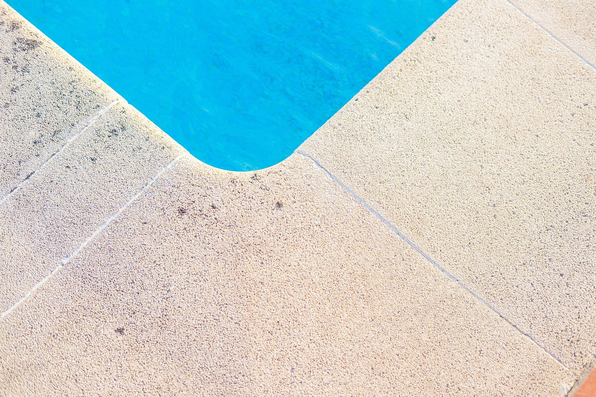 Corner of a blue swimming pool and beige textured concrete patio.