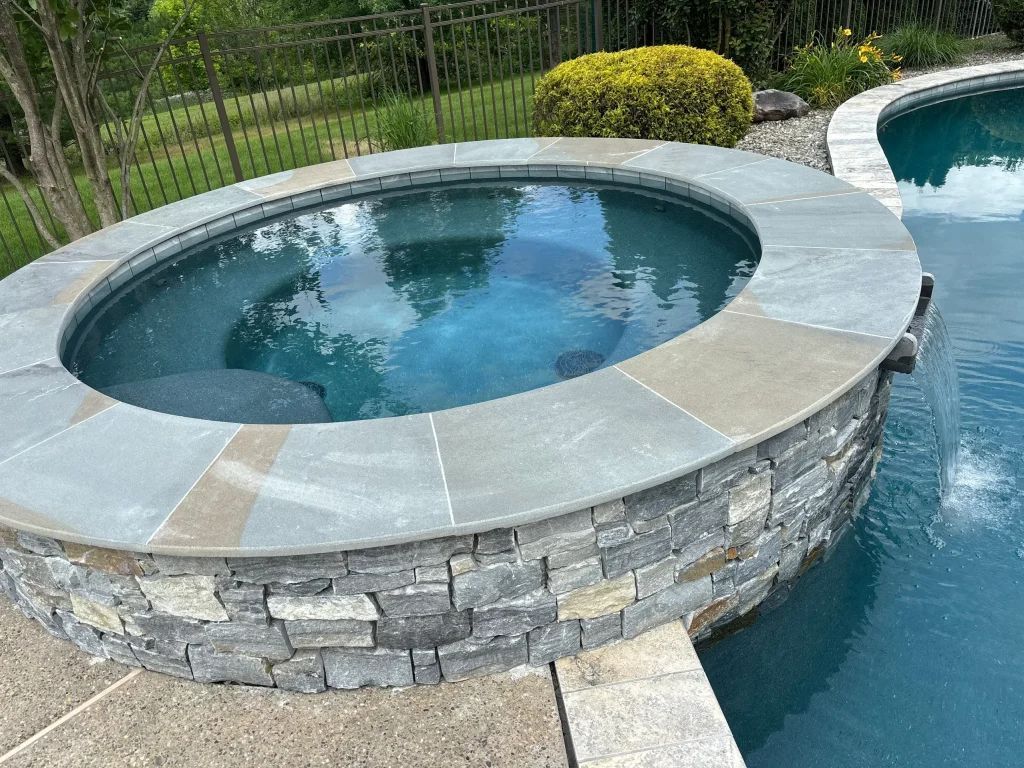 Circular hot tub with stone exterior, next to a swimming pool.