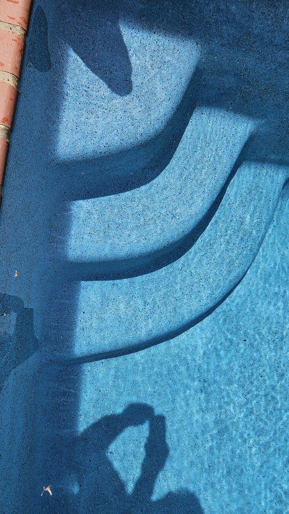Blue pool steps leading into the water with shadows cast on the surface, sunny day.