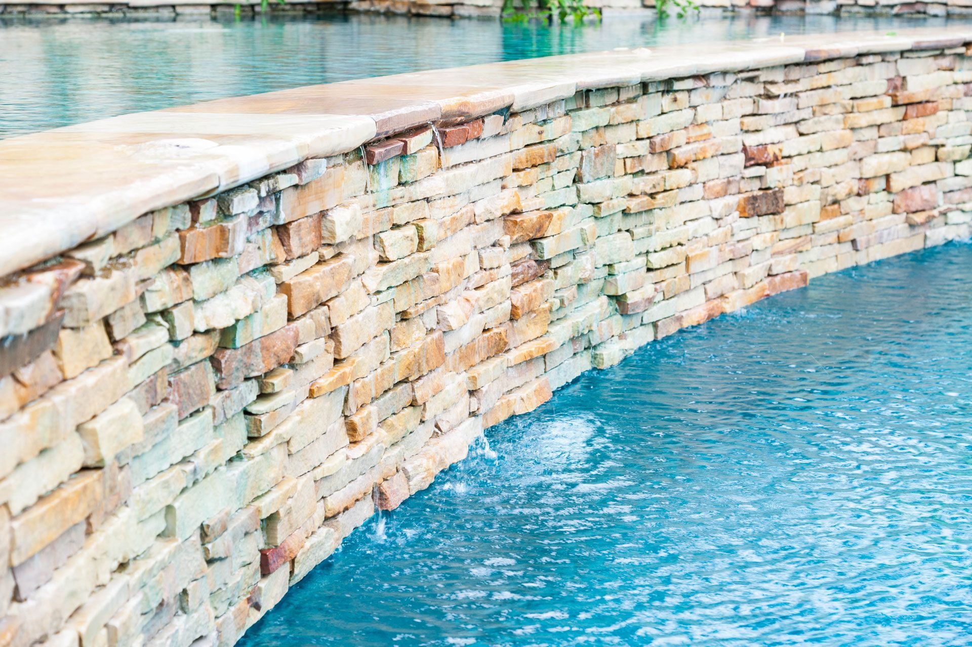 Stone wall curves over clear blue pool water.