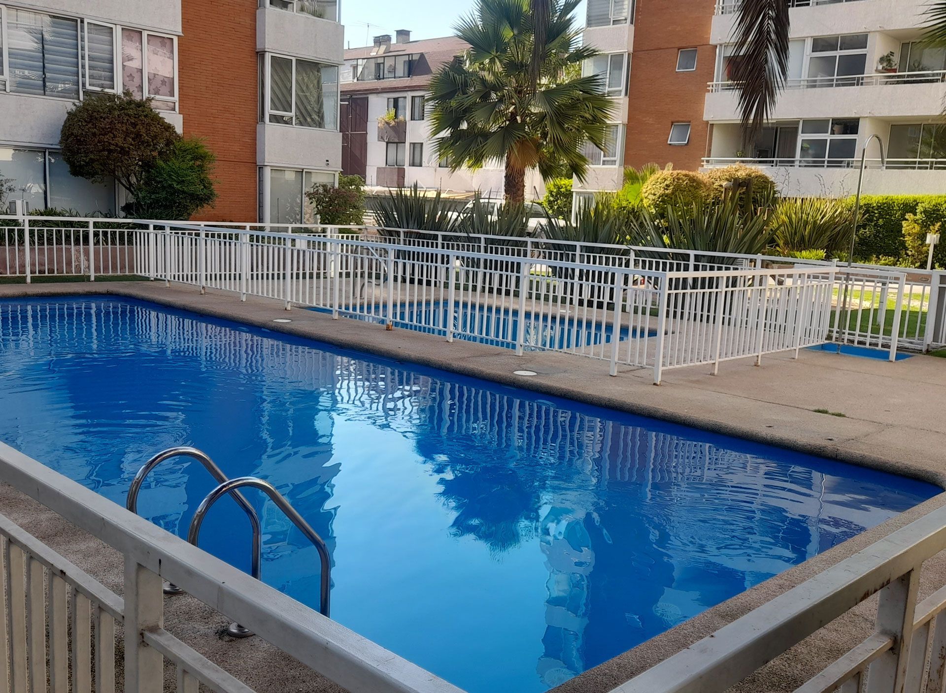 A swimming pool surrounded by a white fence, in front of an apartment building.