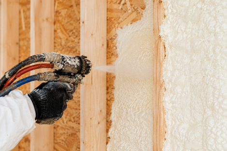 Spray foam getting sprayed from an applicator gun into the cavity of wall studs