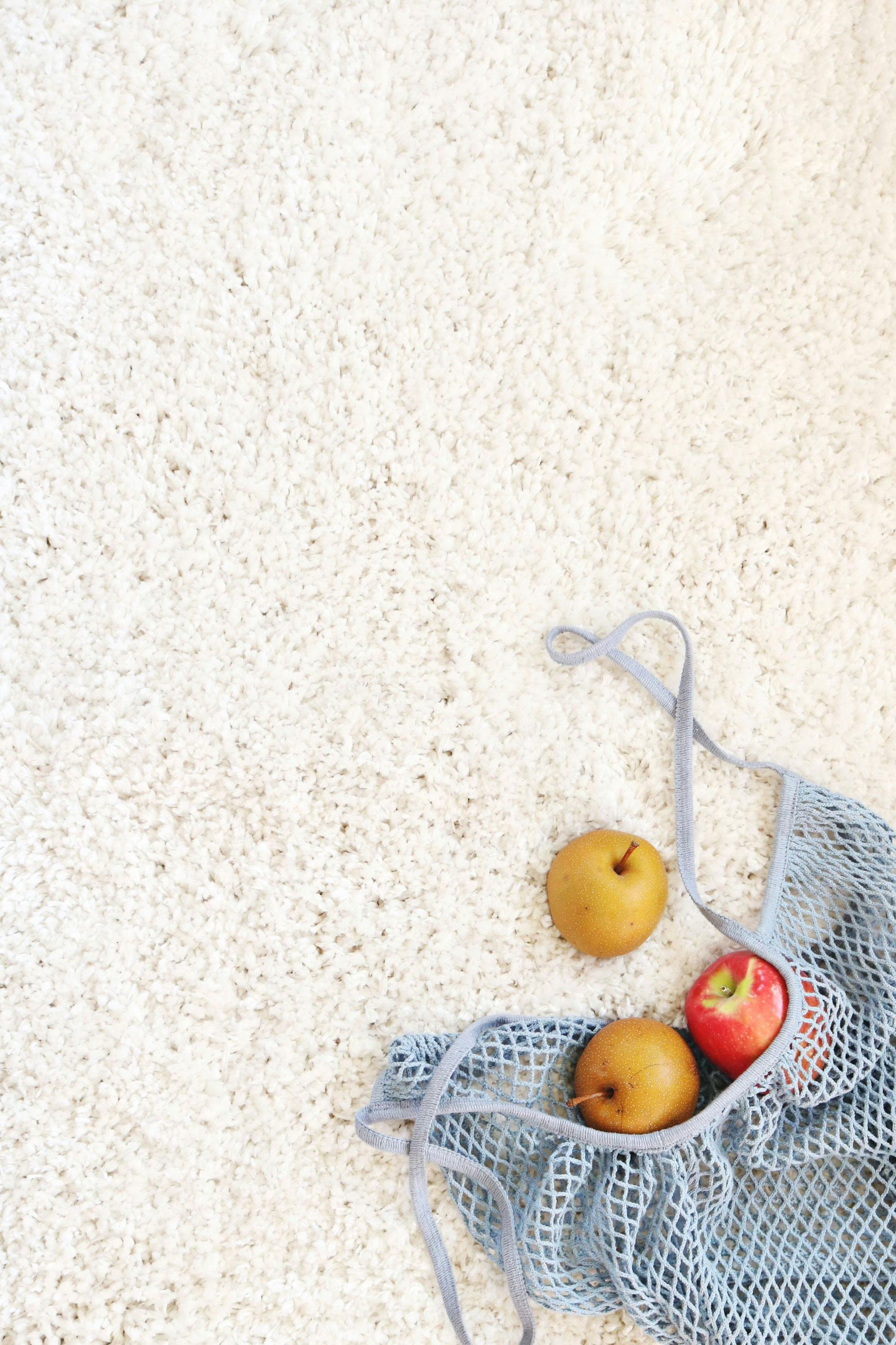 Apples in a blue mesh bag on a textured light surface. One red apple and two brown apples.